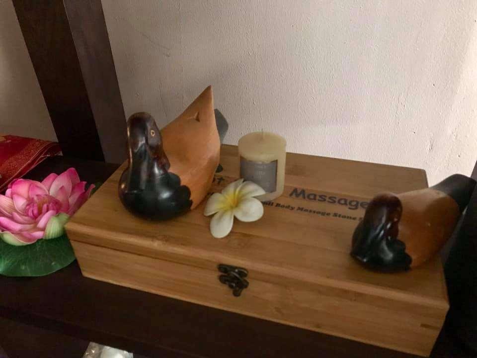 Wooden box with two small duck figurines, a candle, and a white flower on top, with a pink lotus flower beside it.